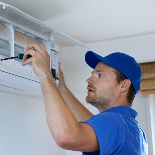 HVAC installer in a blue shirt and hat installing unit.